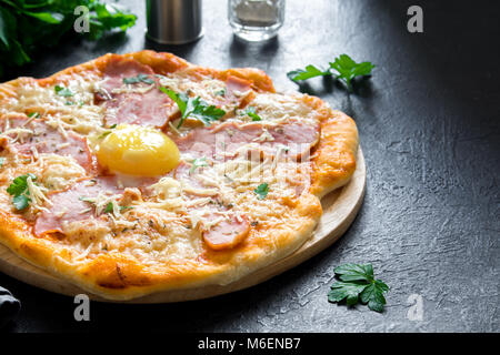 Pizza Carbonara auf schwarzem Stein. Italienische Pizza Carbonara mit Schinken, Ei und Käse, kopieren. Stockfoto