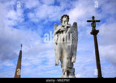 Marmorstatue eines Engels Holding ein Kreuz vor einem blauen bewölkten Himmel in einem Friedhof in Portugal. Stockfoto