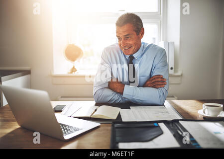 Reifen Geschäftsmann sitzt an seinem Schreibtisch in einem Büro und lächelnd, der an einem Notebook arbeitet Stockfoto