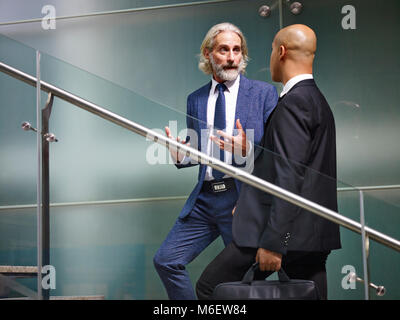 Kaukasische und Latino Führungskräfte ein Gespräch während der aufsteigenden Treppen in einem modernen Bürogebäude. Stockfoto