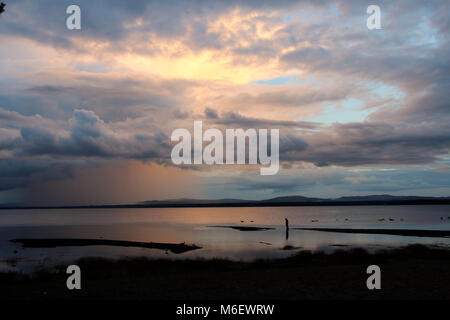 Sonnenuntergang und Wolken spiegeln sich in Orsa See, wo eine Person am Strand steht. Stockfoto