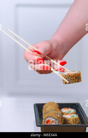Die weibliche Hand mit herrlichen Maniküre nimmt Sushi aus schwarzer Keramik Platte durch hölzerne Stöcke Stockfoto
