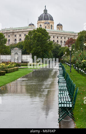 Reihe von leeren Bänken im Volksgarten Wien auf einem nassen Sommer Tag, mit der Burg Theater im Hintergrund Stockfoto