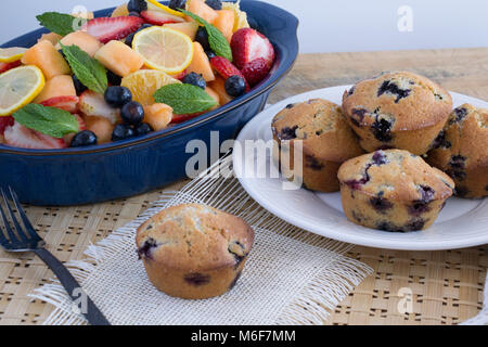 Beginnen Sie den Tag richtig - gebackene blueberry muffins mit einem bunten Schale mit frischem Sommer Obst. Gewürfelt, in Scheiben geschnitten, gebraten, süß, saftig, vollkommene Gesundheit Stockfoto