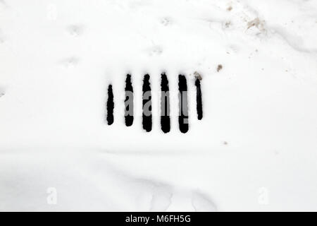 Ein kanaldeckel unter Schnee versteckt, mit einigen Tier Fuß druckt, in Peterborough, Cambridgeshire. Schnee, Peterborough, am 3. März 2018. Stockfoto