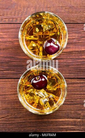 Von whisky Cocktail mit Kirsche in zwei Gläser auf einem hölzernen Hintergrund. Ansicht von oben. Essen Hintergrund Stockfoto