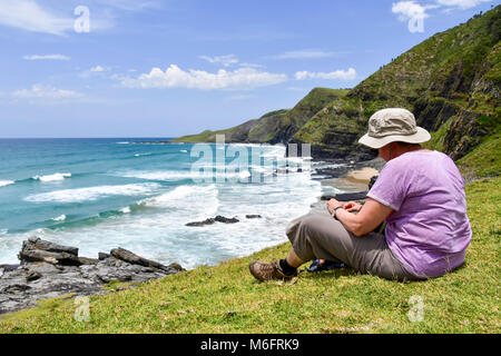 Eine weibliche Wanderer sitzen mit Blick auf die Küstenlinie auf den Spuren von Coffee Bay am Indischen Ozean im östlichen Kap an der wilden Küste von South Af Stockfoto