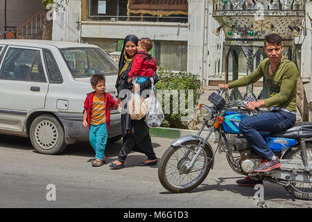 Kashan, Iran - 27. April 2017: muslimische Frau trägt einen schwarzen Tschador, kreuzt die Fahrbahn der Straße mit zwei jungen Kinder eines männlichen. Stockfoto