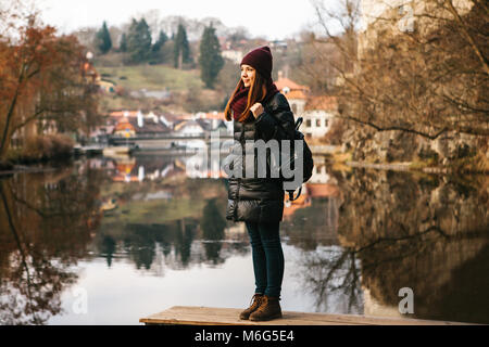 Ein Mädchen mit einem Rucksack auf dem Ufer und genießen die Natur und die Aussicht auf die Stadt Cesky Krumlov in der Tschechischen Republik. Das Konzept der solo Reisen. Stockfoto