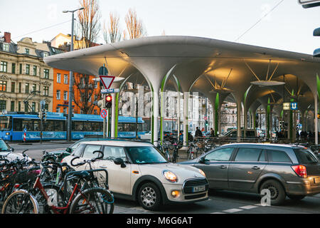 München, 29. Oktober 2017: U-Bahn oder S-Bahn station mit Parkplatz voller Autos und Fahrräder, Straßenbahn und Gebäude im Hintergrund. Stockfoto