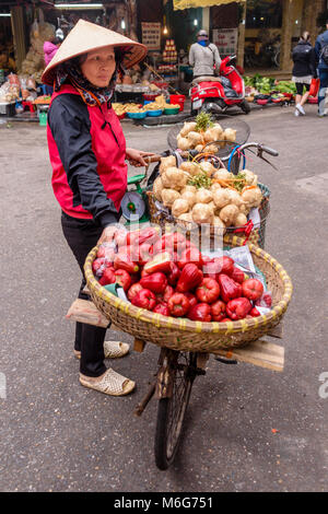 Eine Frau trägt Früchte in Körben zu Ihrem Fahrrad in Hanoi, Vietnam gegurtet Stockfoto