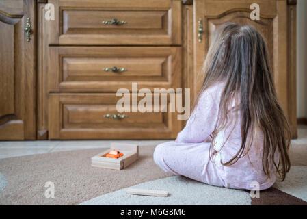 Vier Jahre altes Mädchen im Pyjama sitzt auf Teppich, macht die Garage für Spielzeugauto mit einem Holz- Konstruktor, Entwicklung Stockfoto