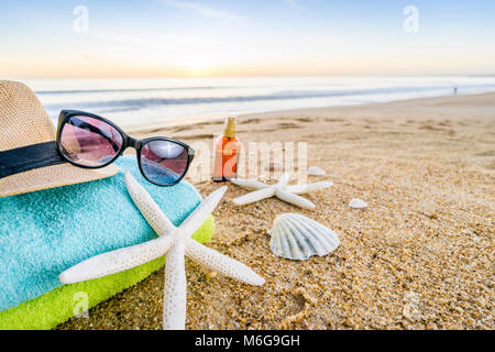 Sommer Accessoires wie Sonnenbrillen, Handtücher, Sonnenhut, Sonnencreme, Muscheln und Seesterne am Sandstrand in Portugal Stockfoto