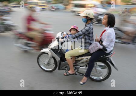 Motorrad im Verkehr mit Mutter fahren junge Schulmädchen auf dem Rücken und kleinen roten Kappe tragen kleine Junge stehend auf vor der Kamera starrt. Stockfoto