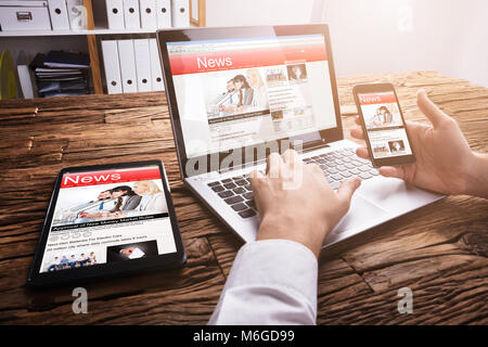 Nahaufnahme der Kaufmann mit Smartphone beim Lesen Online News auf Laptop Stockfoto