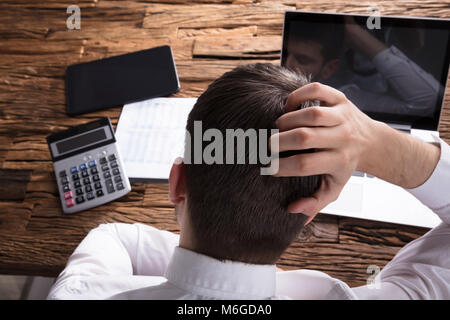 Ansicht der Rückseite ein gestresster Geschäftsmann Kratzen Kopf Vor Laptop Stockfoto