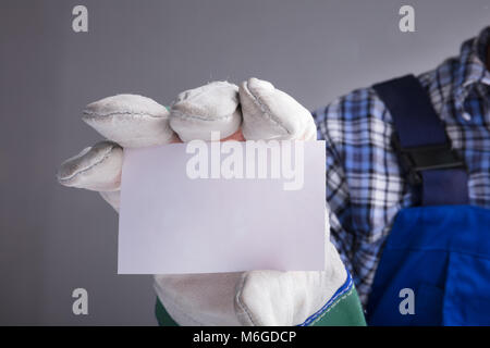 Close-up des Arbeiters Hände mit Handschuhen zeigt eine leere Karte gegen grauer Hintergrund Stockfoto