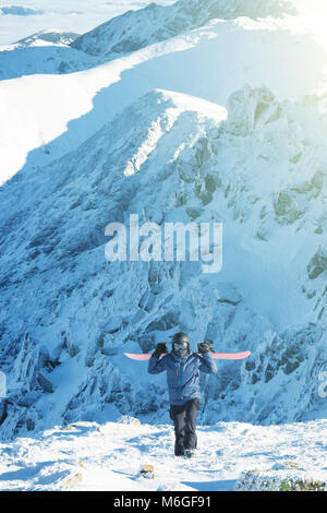 Winter Sport Konzept - jungen männlichen Snowboarder mit seinem snowboard auf seine Schultern nimmt und zu Fuß von Chopok Berg nach oben - draußen geschossen in Jasna Stockfoto