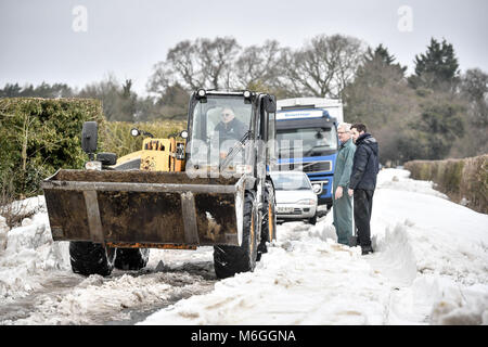 Ein JCB wird verwendet, um die Fahrbahn und Schnee nach Fahrzeuge in Schnee auf Draycott Schließen blockiert wurde, zwischen Draycot Foliat und Ogbourne St George, in der Nähe von Marlborough, Wiltshire, wo die Straße als Ablenkung Route durch die 346 übrigen Eingeschneit verwendet wird. Stockfoto