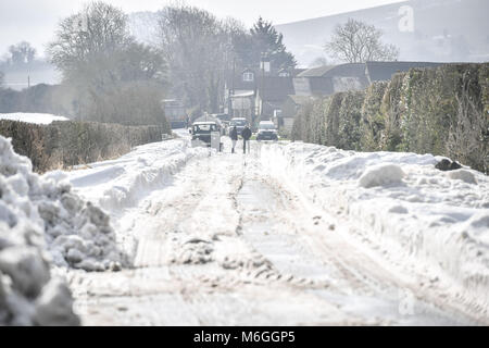 Die Menschen warten geduldig auf eine verschneite Straße als JCB verwendet die Fahrbahn und Schnee nach Fahrzeuge in Schnee auf Draycott Hotel in der Nähe fest geworden ist, zwischen Draycot Foliat und Ogbourne St George, in der Nähe von Marlborough, Wiltshire, wo die Straße als Ablenkung Route durch die 346 übrigen Eingeschneit verwendet wird. Stockfoto