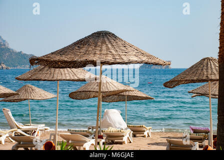 Strohschirme am Strand vor der pulsierenden Kulisse der Meereswellen, die das Wesen eines friedlichen Rückzugs am Meer verkörpern Stockfoto