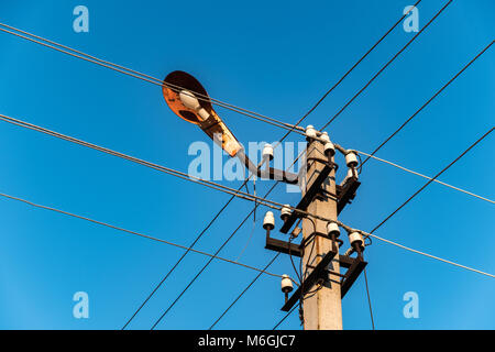 Elektrischer Pol mit Lampe und sich überschneidenden Drähten auf dem Hintergrund des blauen Himmels auf dem Land Stockfoto