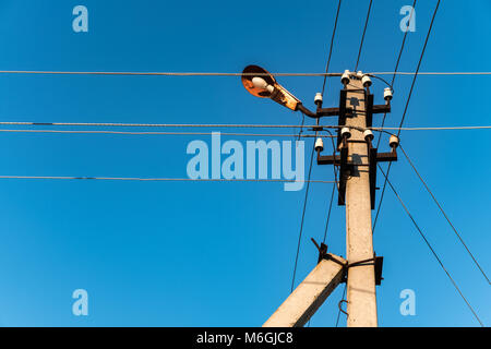 Elektrischer Pol mit Lampe und sich überschneidenden Drähten auf dem Hintergrund des blauen Himmels auf dem Land Stockfoto