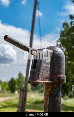 Rostige Metallkonstruktion einer alten Wasserpumpe, die in der ländlichen Straße im Sonnenlicht aufgestellt wurde Stockfoto