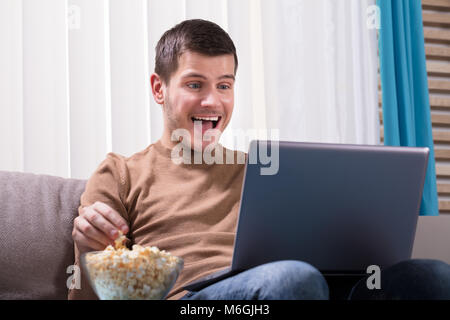 Glückliche junge Mann beobachten Film auf Laptop und Popcorn zu essen zu Hause. Stockfoto