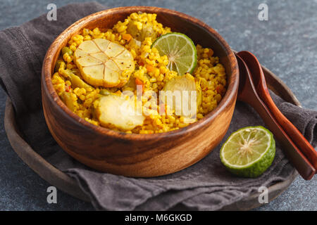 Curry Bulgur mit Gemüse in eine hölzerne Schüssel. Dunkler Hintergrund, vegane Mahlzeit Konzept. Stockfoto