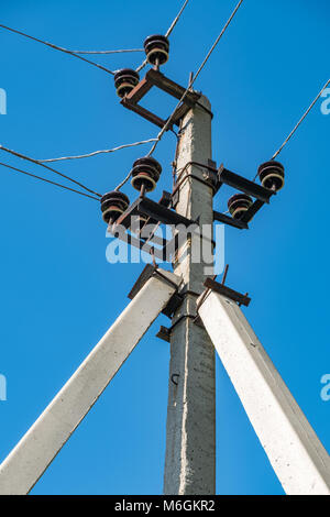 Elektrischer Mast und sich kreuzende Drähte auf dem Hintergrund des blauen Himmels auf dem Land Stockfoto