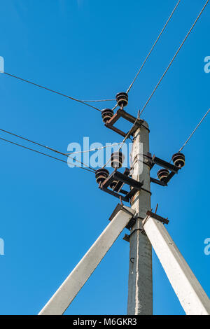 Elektrischer Mast und sich kreuzende Drähte auf dem Hintergrund des blauen Himmels auf dem Land Stockfoto