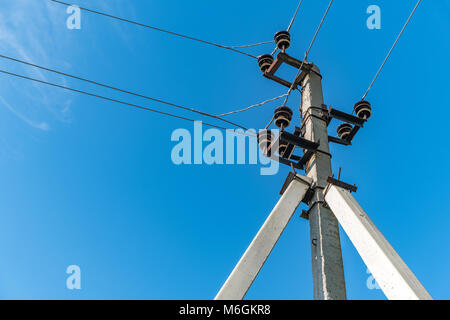 Elektrischer Mast und sich kreuzende Drähte auf dem Hintergrund des blauen Himmels auf dem Land Stockfoto