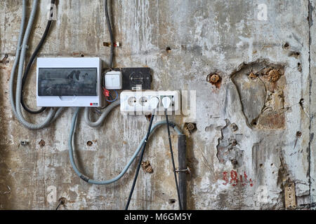 Alte abblätternde Betonwand, die mit Kabelzubehör, Elektroverteilern und Steckdosen in einer Werkstatt bedeckt ist Stockfoto