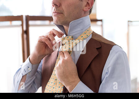 Mann verknoten seine Krawatte beim Dressing in einer formalen Hemd und Weste in der Nähe zu sehen, der seine Hände Stockfoto