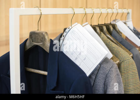 Maßgeschneiderte Jacken auf Bügeln hängend auf einer Schiene mit Ihrer Bestellung Informationen und Messungen zugeschnitten Stockfoto