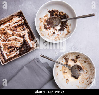 Schokoladenpudding Reste auf einem grauen strukturierten Hintergrund mit mapkin Löffeln und Schalen Stockfoto