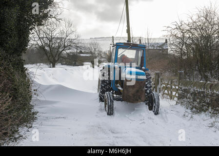 Traktor eine Straße mit tiefen Schneewehen in der englischen Landschaft freigeben, während die "Tier aus dem Osten' 2018. Stockfoto