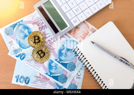 Zwei goldene Bitcoins, Rechner, Journal und Stift auf türkisch Papier Banknoten, Ansicht von oben Stockfoto