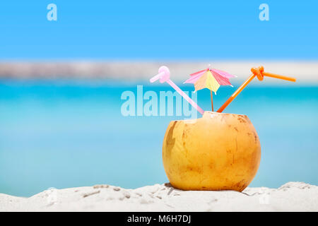 Nahaufnahme Bild einer Kokosnuss mit zwei strohhalme und bunten Sonnenschirm am Strand, Sommerurlaub Konzept, selektive konzentrieren. Stockfoto