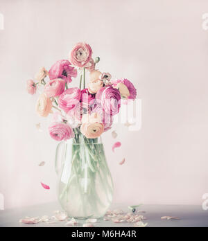 Pastellfarben ranunculus blumen blumenstrauss mit fallenden Blütenblättern in Glass Vase auf dem Tisch, Vorderansicht Stockfoto