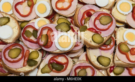 Open-face-Sandwiches als gastronomisches Hintergrund. Bunte Textur aus Scheiben französisches Brot mit Schinken, Käse, hart gekochten Eiern, Paprika und Gurke. Stockfoto