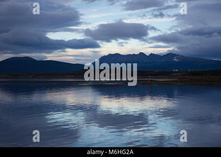 Sonnenuntergang in Ushuaia mit dramatischen Grau und Blau Wolken über Blau und Braun mountins Ausläufern. Eine Reflexion der Wolken ist im Wasser in t Stockfoto