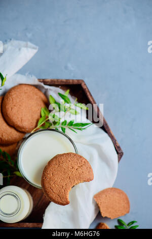 Cookies mit bissspuren, ein Glas Milch und kleine grüne Blätter Einrichtung auf einem Stein Hintergrund mit weißer Bettwäsche Serviette. Gesundes Frühstück Konzept mit Cop Stockfoto