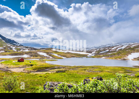 Rote Hütte an einem Bergsee, Norwegen, umgeben von schneebedeckten Bergen im Sommer, Nord-Norwegen, Vikafjell Stockfoto