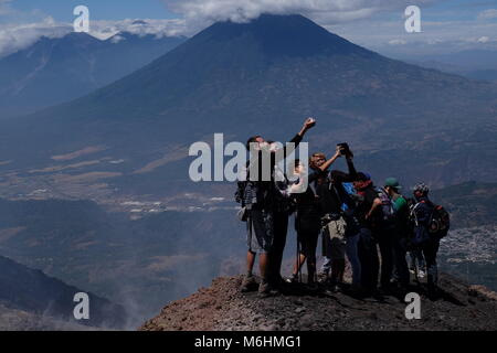 Touristen nehmen selfies nach Erreichen der Spitze des Vulkans Pacaya mit Fuego im Hintergrund in Guatemala. Stockfoto