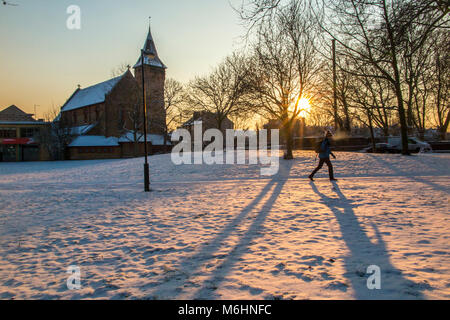 Eine Person Wanderungen durch den Schnee Kirchhof bei Sonnenaufgang abgedeckt Stockfoto