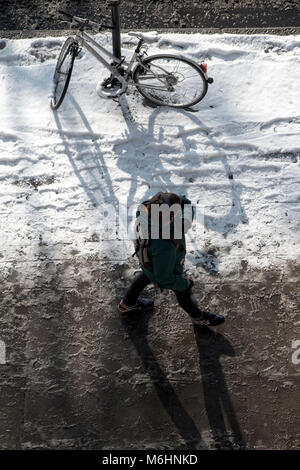 Zu Fuß durch den Schnee in Central London, Blick von oben nach unten mit einem abgestellten Fahrrad, angekettet an einen Laternenpfahl Stockfoto