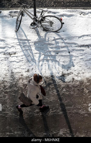 Zu Fuß durch den Schnee in Central London, Blick von oben nach unten mit einem abgestellten Fahrrad, angekettet an einen Laternenpfahl Stockfoto