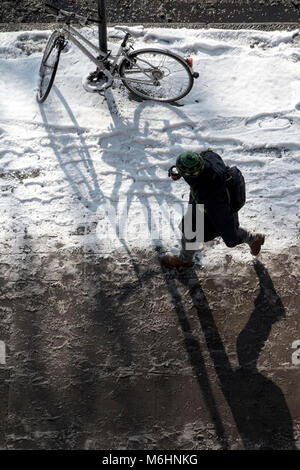 Zu Fuß durch den Schnee in Central London, Blick von oben nach unten mit einem abgestellten Fahrrad, angekettet an einen Laternenpfahl Stockfoto